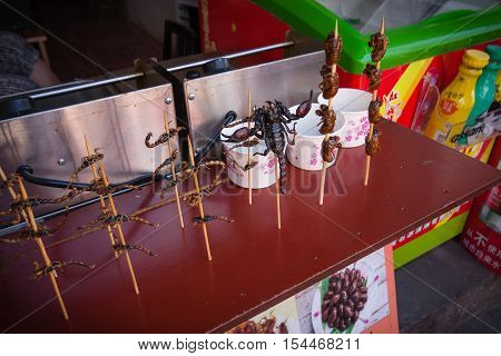ZHUJIAJIAO CHINA - AUGUST 30 2016: Scorpions insects and bugs on spits are offered to shopping tourists as food by a vendor in the market street stall in Zhujiajiao China on August 30 2016.