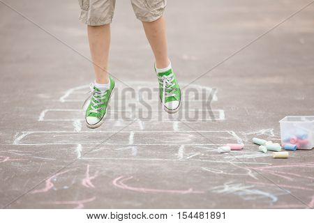 Closeup of boy's legs and hopscotch drawn on asphalt. Child playing hopscotch on playground outdoors on a sunny day. outdoor activities for children.