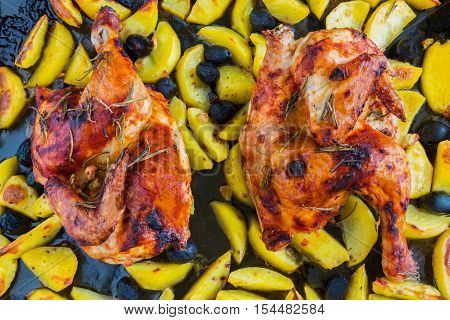 Roasted chicken halves black baking sheet potatoes and olives cooked in oil top view.