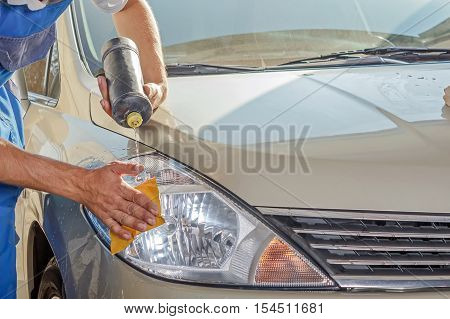 The worker polishes optics of headlights of the car to restore gloss and transparency