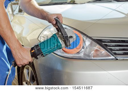 The worker polishes optics of headlights of the car with the electric tool.