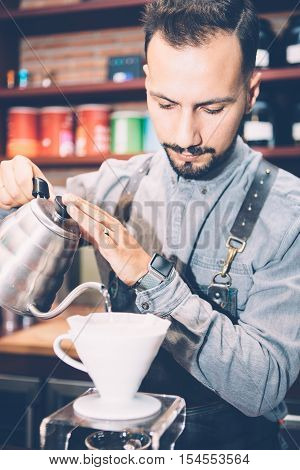 Portrait of professional coffeemaker pouring hot water from kettle in coffee machine