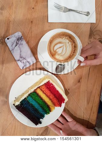 Female hand holding coffee cup and cake plate with smartphone on one side in a cafe