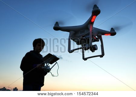 Man operating drone flying or hovering by remote control in sunset.
