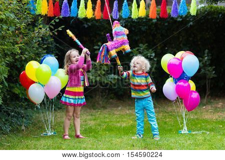 Kids birthday party. Group of children hitting pinata and playing with balloons. Family and friends celebrating birthday outdoors in decorated garden. Outdoor celebration with active games.