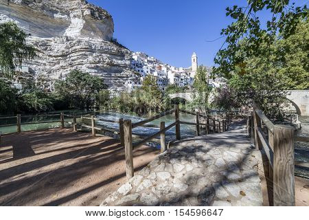 Alcala del Jucar Spain - October 29 2016: Small wooden bridge over the river Jucar located in the central part of the town the fund for the Church of San Andres styles late Gothic and Neoclassic take in Alcala of the Jucar Albacete province Spain
