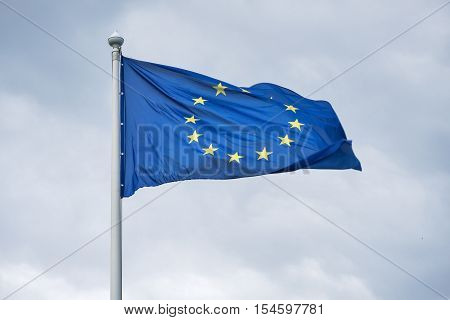 The flag of the European Union fluttering on wind against the background of gray clouds.