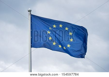 The flag of the European Union fluttering on wind against the background of gray clouds.