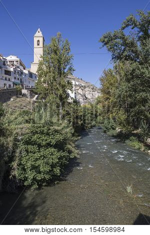 Alcala del Jucar Spain - October 29 2016: Clear waters of the river Jucar on the Roman bridge to the left the Church of San Andres of styles late and neoclassic Gothic take in Alcala of the Jucar Albacete province Spain