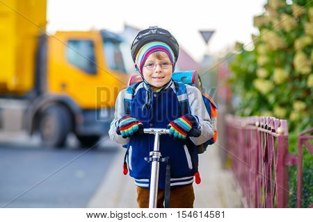 Active school kid boy in safety helmet riding with his scooter in the city. Happy child in colorful clothes biking on way to school. Safe way for kids outdoors to school.