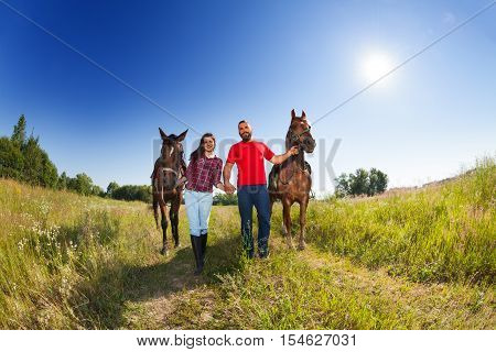 Loving couple walking with their bay horses at sunny day