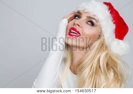Beautiful sexy blonde female model dressed as Santa Claus in a red cap with a tassel at the White fur lovely makeup sensual lips, beauty photo Christmassy, Christmas
