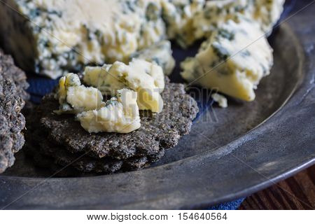 Mature English Stilton cheese and charcoal crackers on a pewter plate shot with low key light