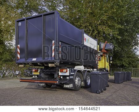 SNEEK, THE NETHERLANDS - OCTOBER 29, 2016: A recycling truck picking up two grey bins from a row of bins on the street. With a side loader the driver operates the mechanical gripper from his cabin.