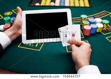 casino, online gambling, technology and people concept - close up of poker player with playing cards, tablet and chips at green casino table. first-person view. two aces, a winning combination