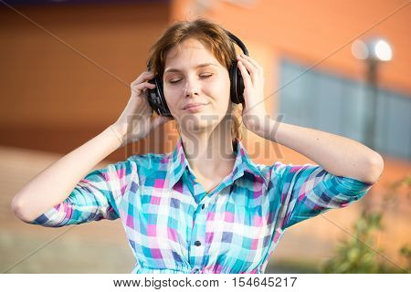 Young beautiful girl listening to music player on the street. tudent woman at campus park.