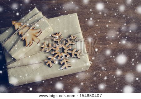 Kraft Boxes with Gifts Decorated with Wooden Snowflake Christmas Tree and Jute on Wooden Background. Vintage Image with Drawn Snowfall. Christmas in Rustic Style. View from above with copy space.