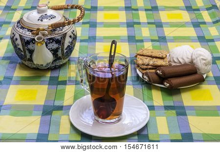 On the table mishandled colored tablecloth. On the tablecloth is a glass cup with tea tea and sweets in the basket are