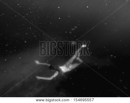 Woman swimming deep underwater black and white.