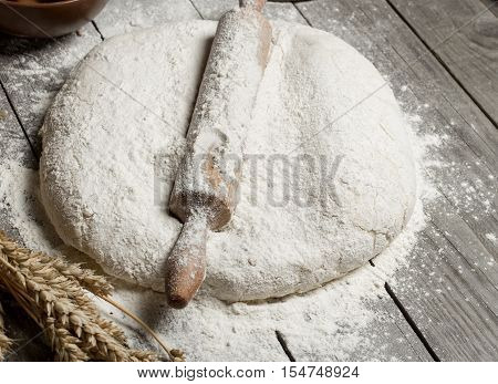 Rolling pin with flour and wheat on wooden table. Bakery background