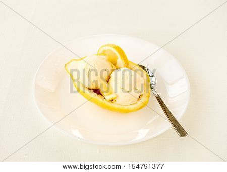 Half of an Amalfitano lemon filled with homemade lemon ice cream served on a white porcelain plate with spoon. An ivory colored tablecloth as background.