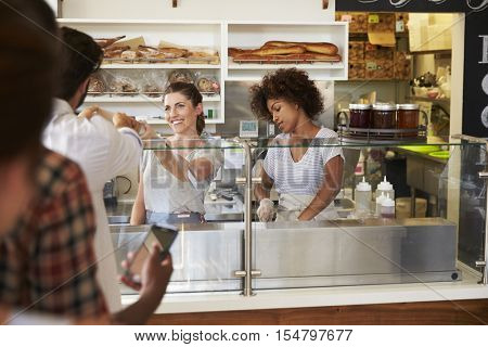 A queue of customers served by two women at a sandwich bar
