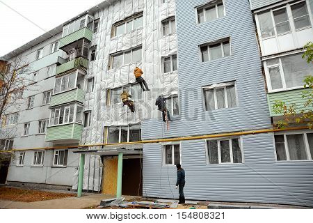 Repair and restoration of a facade of a building. Home facade insulation. Group of workers installs panels siding on a wall of a house