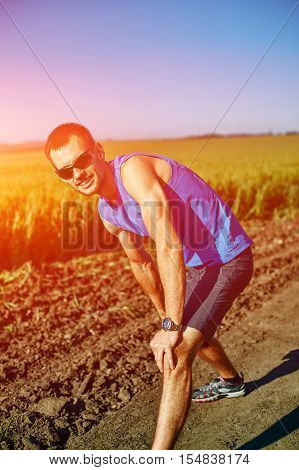 man runner athlete warming up before jogging along a green field in the early morning. man lunged forward on one knee. athlete feels pain in knee. man fitness sunset jogging workout wellness concept.