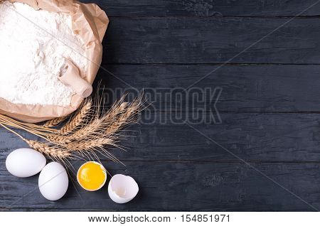 Baking background. Flour in paper bag wheat and eggs on dark wooden table. Ingredients for cooking homemade baking. Top view. Copy space
