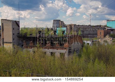 Abandoned factory of synthetic rubber overgrown by trees, ruins of buildings and cooling towers