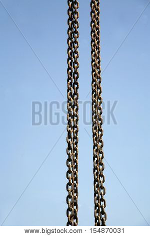 Long meatal chains hanging vertically against blue sky