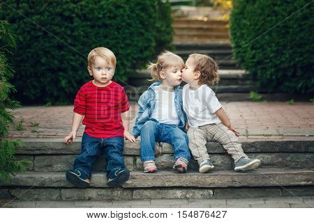 Group of three cute funny adorable white Caucasian children toddlers boys girl sitting together kissing each other love friendship childhood concept best friends forever