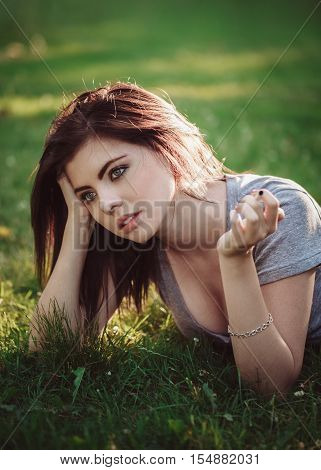 Closeup portrait of white Caucasian beautiful young brunette woman lying on ground grass smoking cigarette toned with filters bad unhealthy habit lifestyle concept