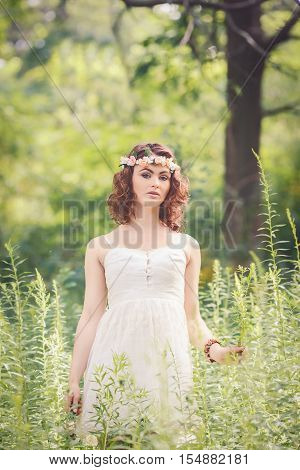 Beautiful white Caucasian girl with hazel eyes long wavy curly hair and flowers chaplet on head. Attractive young woman model in park outside country village hippie style
