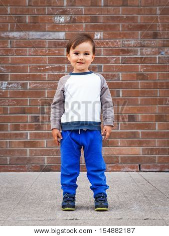 Portrait of a cute adorable little boy toddler two or three years old standing by brick wall and smiling laughing posing outside in the street