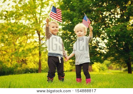 Happy adorable little blond Caucasian girl and boy smiling laughing holding hands and waving American flag outside celebrating 4th july Independence Day Flag Day concept