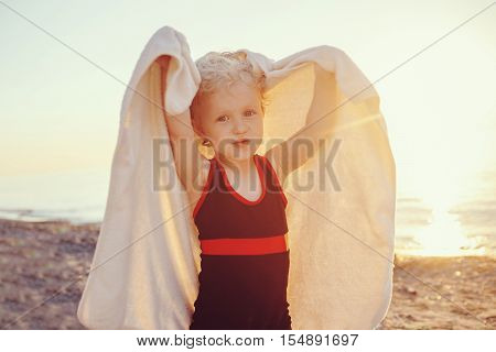 Portrait of cute adorable happy smiling toddler little girl with towel on beach making poses faces having fun emotional face expression lifestyle sunset summer mood toned