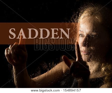 sadden written on virtual screen. hand of young woman melancholy and sad at the window in the rain