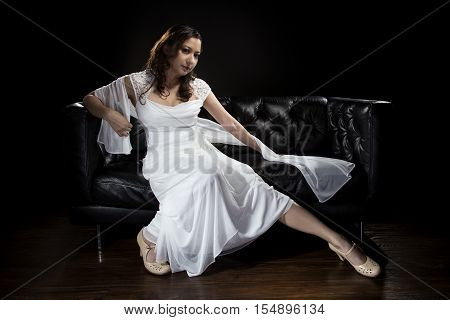 Bridal modeling modern fashion trend of simple but elegant thin wedding dress in retro or art deco style. Bride on couch with shoulder scarf and bridal gown.
