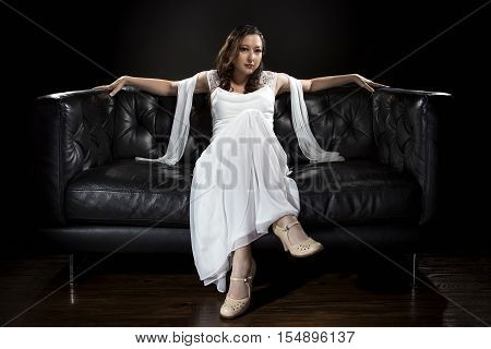 Bridal modeling modern fashion trend of simple but elegant thin wedding dress in retro or art deco style. Bride on couch with shoulder scarf and bridal gown.