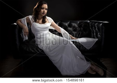Bridal modeling modern fashion trend of simple but elegant thin wedding dress in retro or art deco style. Bride on couch with shoulder scarf and bridal gown.