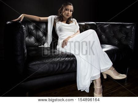 Bridal modeling modern fashion trend of simple but elegant thin wedding dress in retro or art deco style. Bride on couch with shoulder scarf and bridal gown.