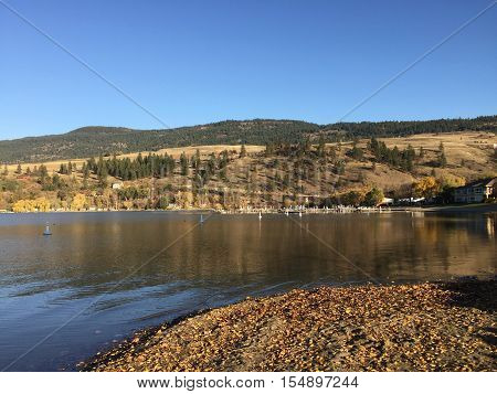 Blue sky and calm lake with dock and hills in background.