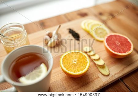 health, traditional medicine, folk remedy and ethnoscience concept - cup of ginger tea with honey, citrus and garlic on wooden background