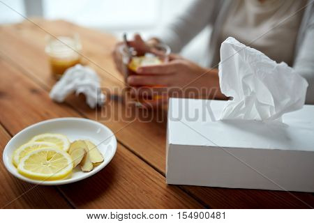 health, traditional medicine and ethnoscience concept - ill woman drinking tea with lemon, honey and ginger and paper wipes box on wooden table