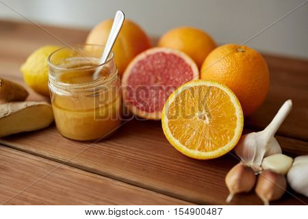 traditional medicine, cooking, food and ethnoscience concept - honey, citrus fruits with ginger and garlic on wooden table