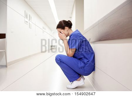 people, medicine, healthcare and sorrow concept - sad or crying female nurse at hospital corridor