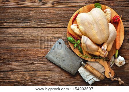 Raw chicken with cleaver and spices on wooden background