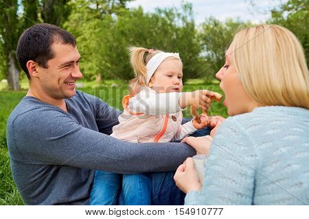 Happy Family Picnicking In The Park. Daughter Feeding Mother Playfully.