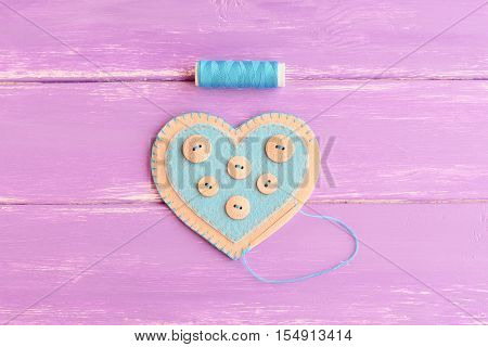 How to sew a felt heart decor. Step. Join the felt edges of felt heart with blue thread. Blue thread, needle on wooden background. DIY idea for Valentine's day, wedding, mother's day. Top view